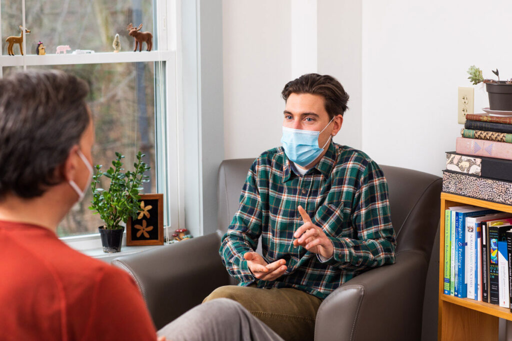Young man in face mask talking to unrecognizable doctor
