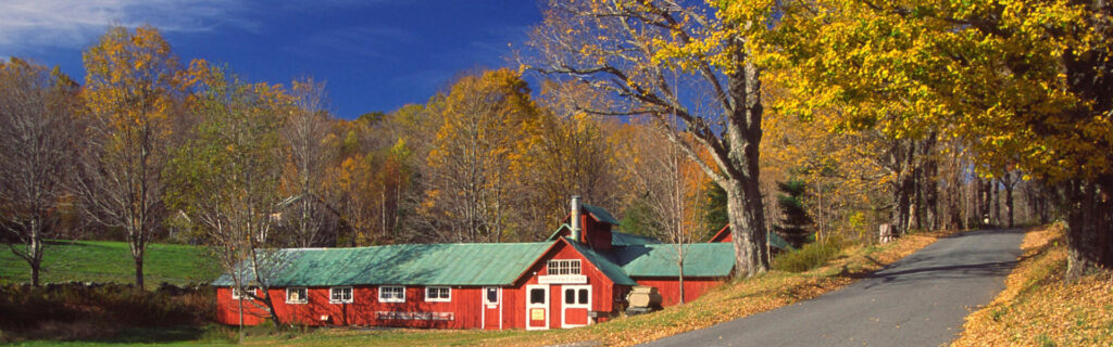 a picturesque red building with a green roof emulates the feel of an old farm building. there are trees with autumn foliage all around and a road passes by